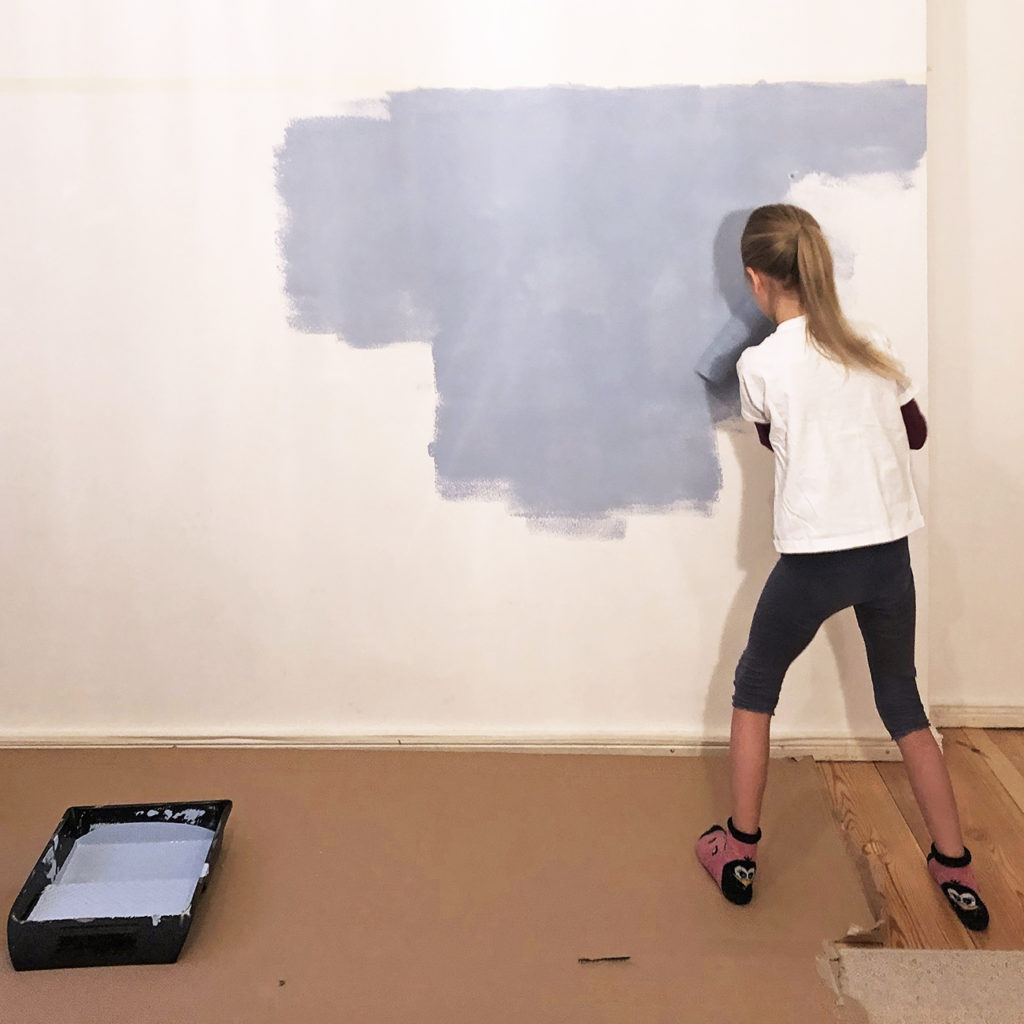 Ein Kind setzt die Ergebnisse aus dem Workshop um und streicht mit blauer Farbe eine Wand.