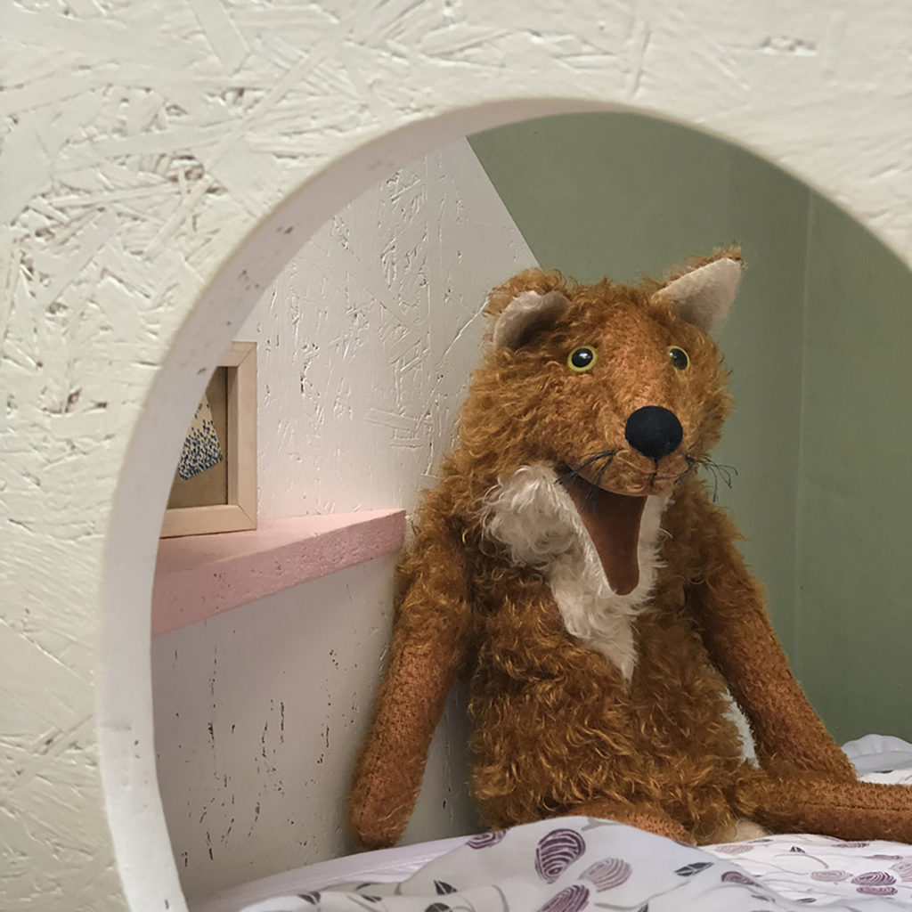 Im Kinderzimmer guckt ein Stofftier durch das rundes Loch eines Kinder Betts.