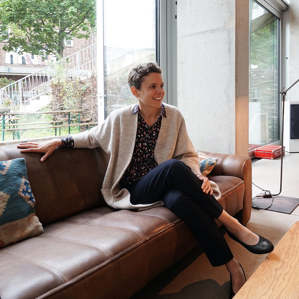 Ein Portraitbild von Anna Brack auf einem Sofa sitzend, die in ihrem Krativbüro individuelle Raumgestaltung macht.